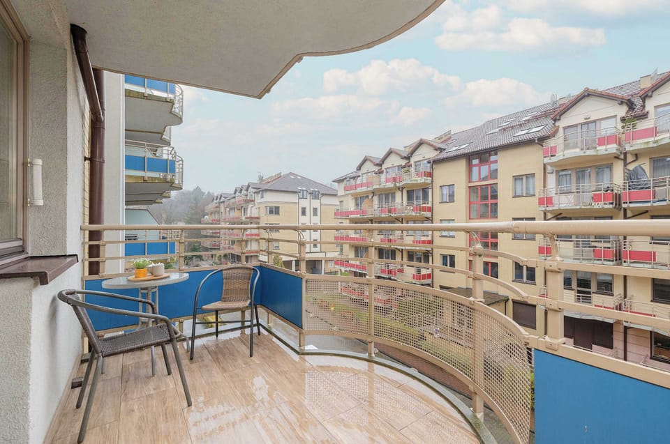 A private balcony with metal railings, offering views of nearby apartment buildings and greenery.