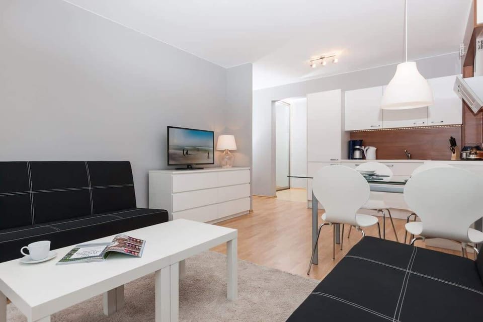A wider angle of the previous room showing the same black sofas and coffee table. You can also see the TV on a white console, and more of the dining area in the background.