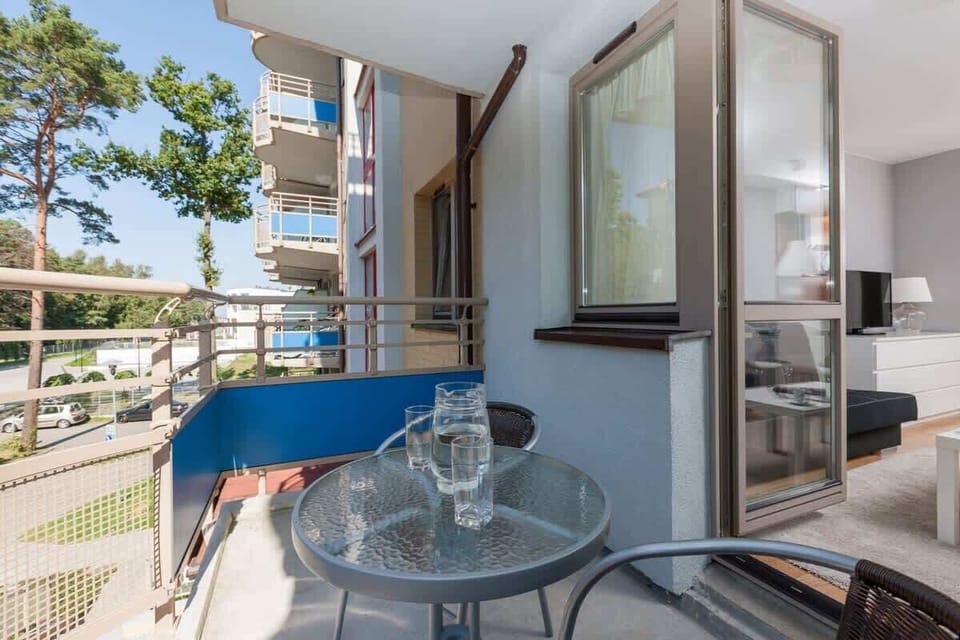 One image shows a balcony from a modern, multi-story residential building. The balcony overlooks a green area and a street with parked cars. There are flower pots along the railing, and the building itself has a well-maintained, contemporary façade.