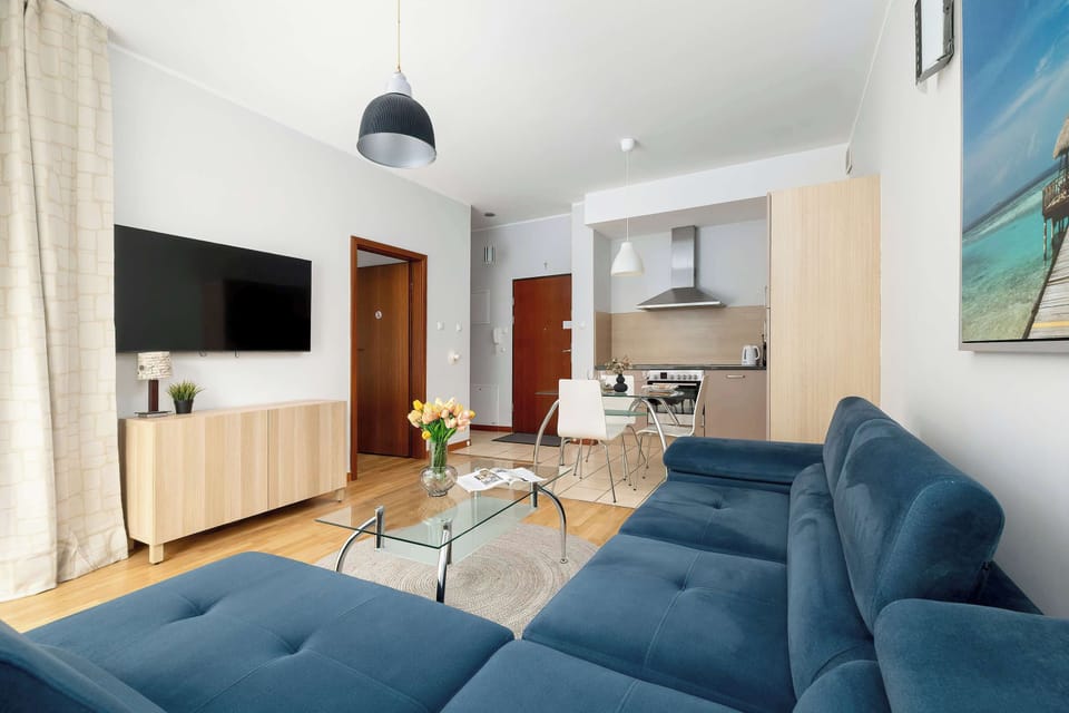 A cozy living room with a blue sectional sofa and a TV. Large windows bring in natural light, making it feel inviting.