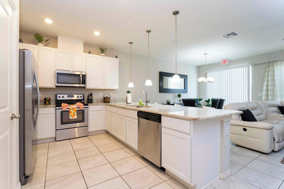 Bright, modern kitchen with white cabinets, granite counters, and stainless-steel appliances. A spacious island and pendant lights make meal prep a social, stylish hub.