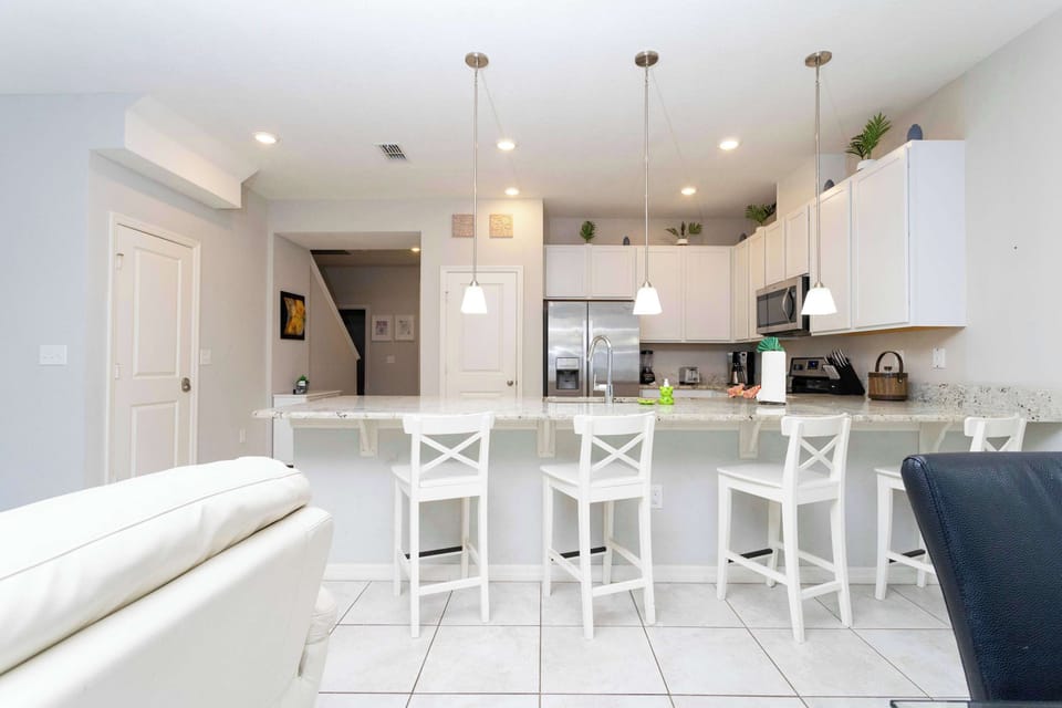 Open kitchen with granite island, white cabinets, and four white bar stools-ideal for casual meals.