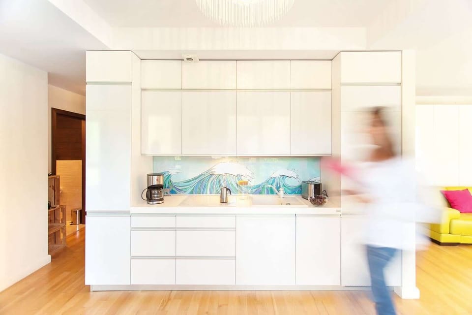 A bright, open kitchen with white cabinetry and a central island. The space has a light and airy feel, with a pop of color from the blue backsplash.