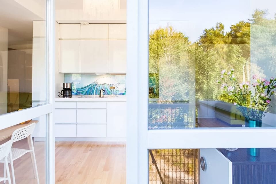 A view from inside looking out through glass doors onto a balcony surrounded by greenery. The doors allow plenty of light to fill the room, connecting the indoor and outdoor spaces.