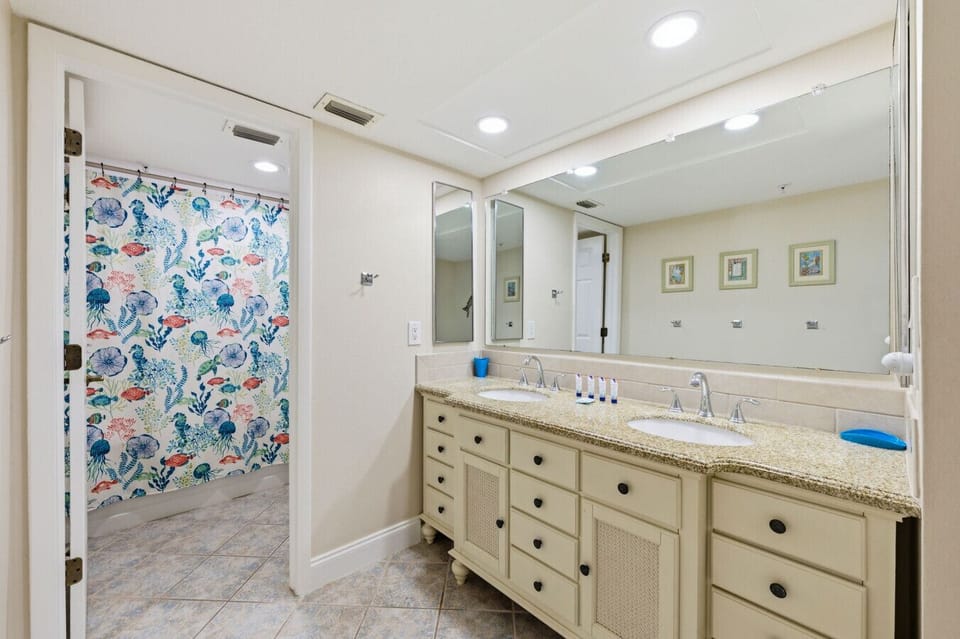 Spacious Coastal Vacation Condo Primary Bathroom Featuring a Double-Sink Vanity, Granite Countertops, Large Mirror, Ample Storage, and a Shower and Bathtub Area