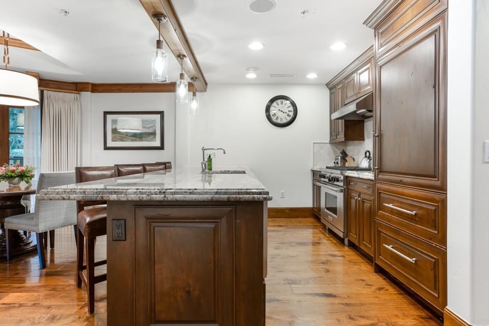 Granite countertop island with built-in sink faces leather barstools and dark wood cabinetry in the kitchen.