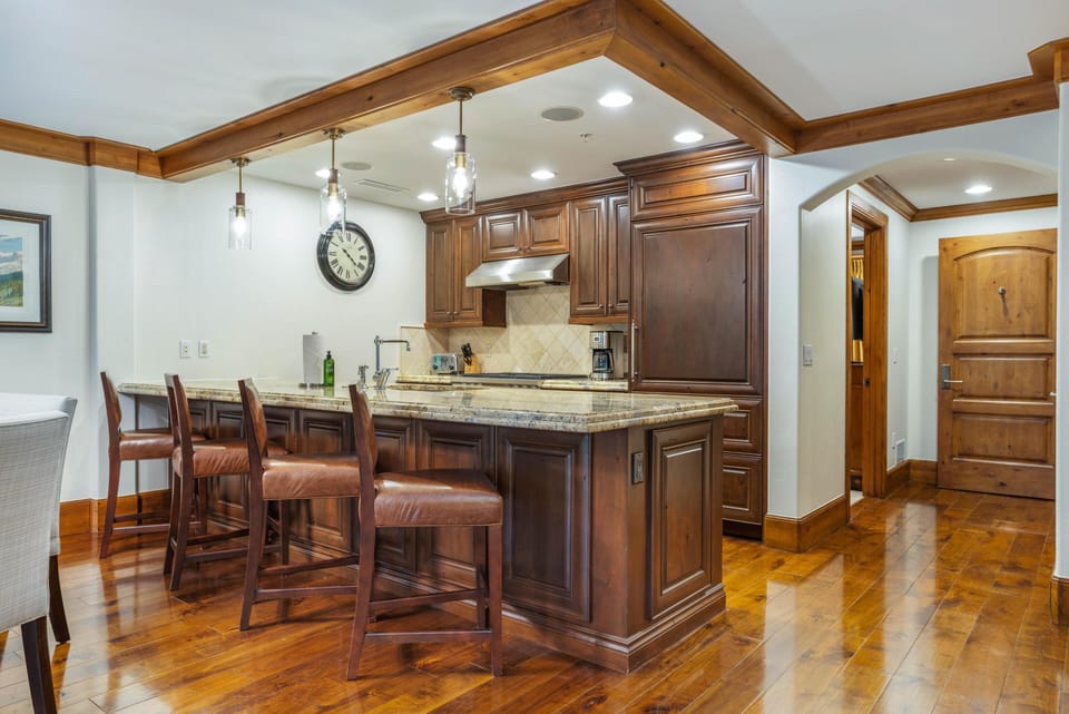 Dark wood kitchen island with granite countertop and leather barstools under glass pendant lights.