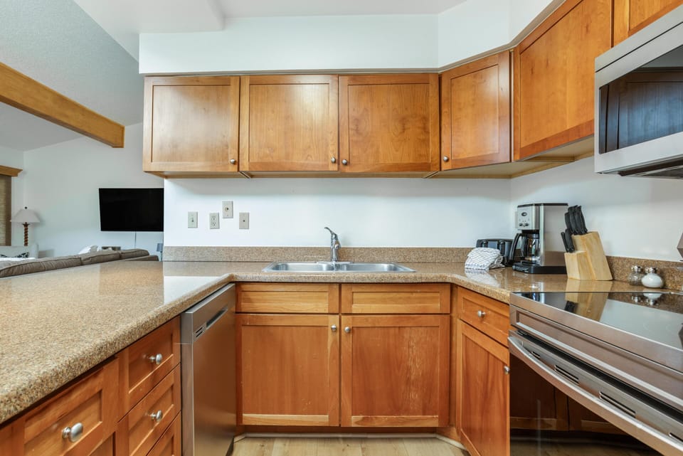 Kitchen corner featuring honey-toned wood cabinets, granite countertops, stainless steel sink, and modern appliances.