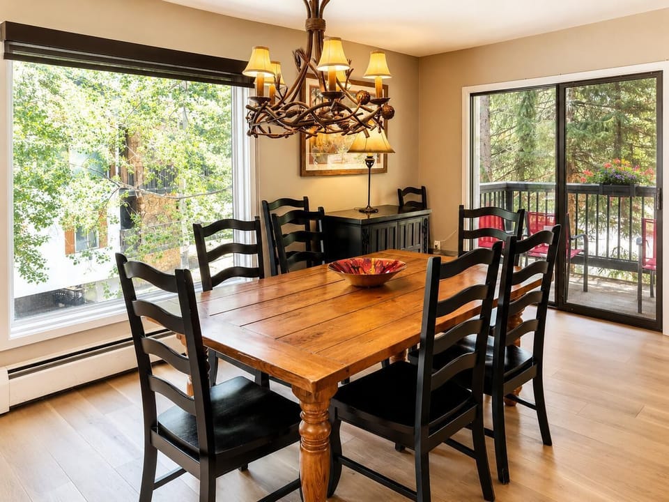 Dining area with a solid wood table, six black ladder-back chairs, and antler-inspired chandelier above.
