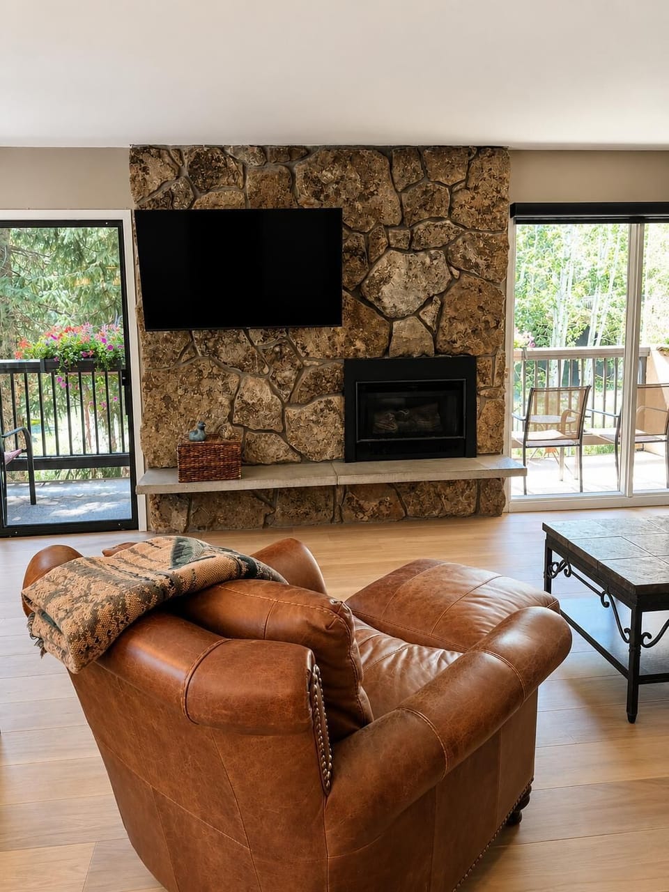 Leather armchair faces a stone fireplace with mounted flat-screen TV, flanked by sliding glass doors to balconies.