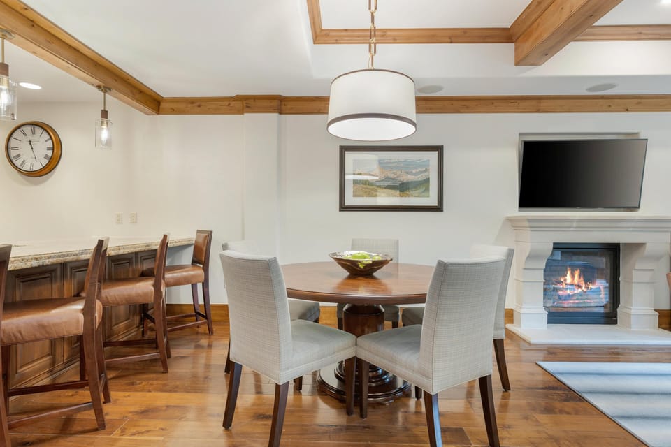 Round wood dining table surrounded by four gray upholstered chairs beneath a drum pendant light.