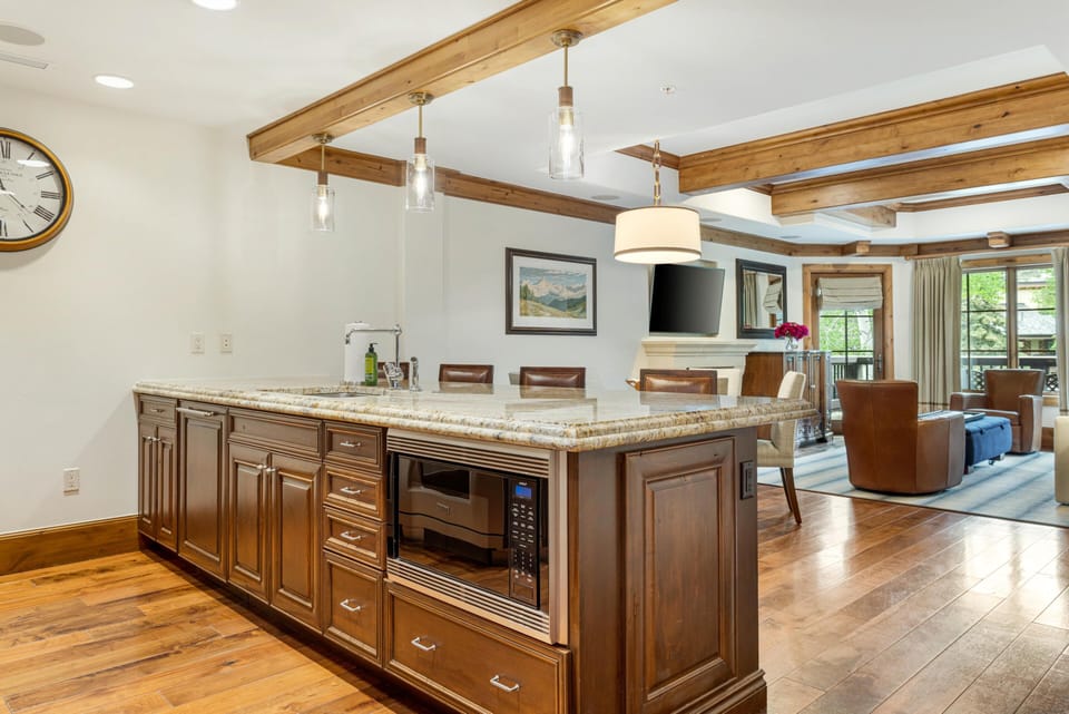 Granite-topped kitchen island with built-in microwave and dark wood cabinets under clear glass pendant lights.