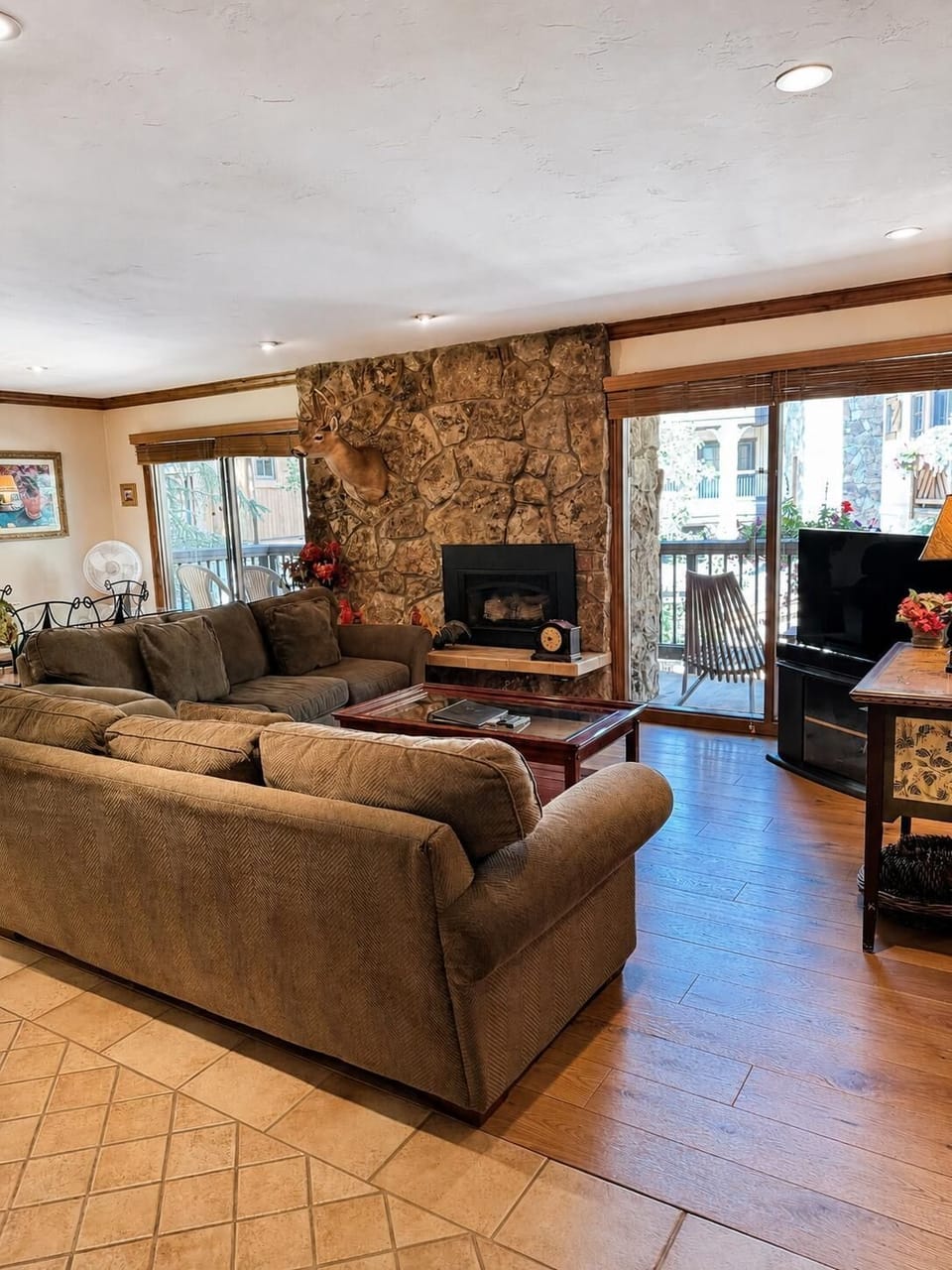 Living room features a stone fireplace with mounted deer head, plush sectional, and sliding doors to the balcony.