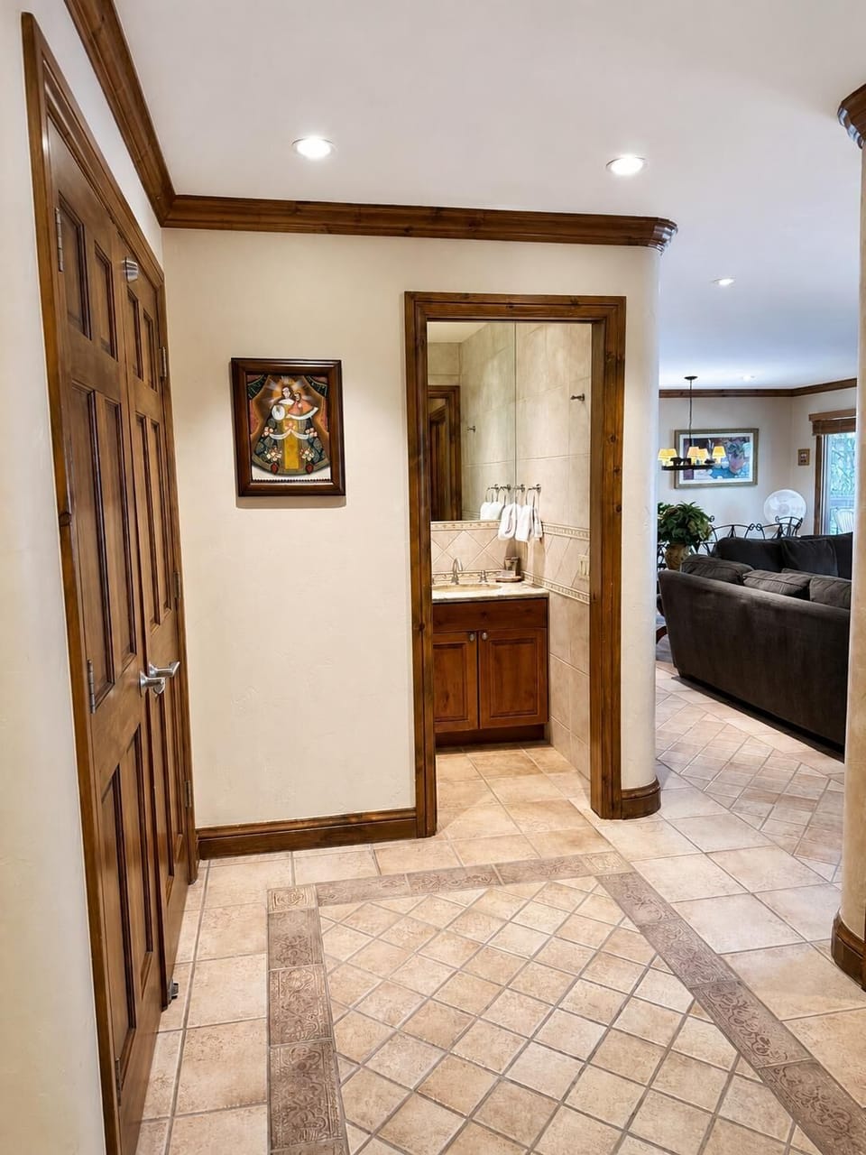 Entryway with decorative tile flooring, wooden trim, and a small bathroom featuring tiled walls and a wood vanity.