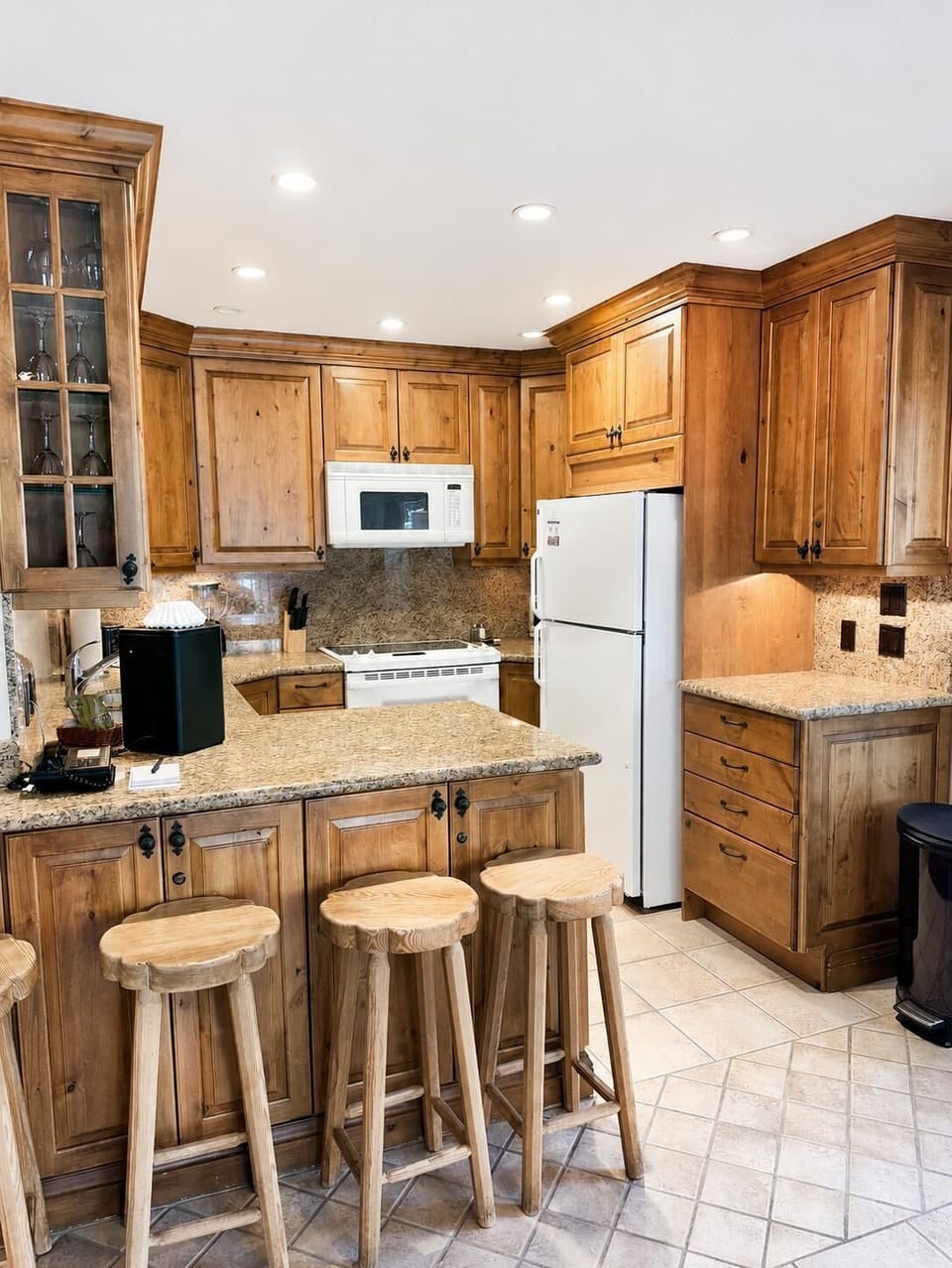 Knotty pine cabinetry surrounds the kitchen with granite counters, a white stove, and three wooden bar stools.