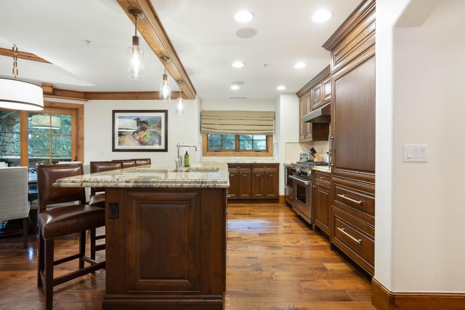 Dark wood cabinetry and hardwood floors complement granite countertops and leather bar stools in the kitchen.
