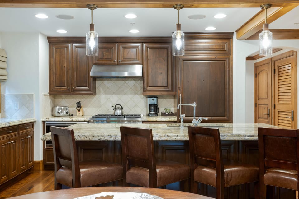 Three glass pendant lights illuminate the granite kitchen island with built-in sink and high-back leather stools.