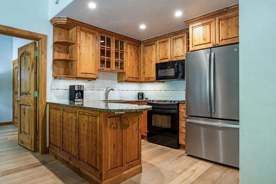 Kitchen features knotty wood cabinets, granite countertops, stainless steel fridge, and black oven with microwave.