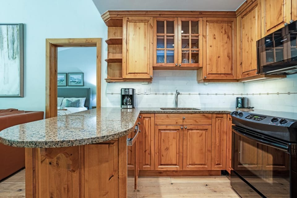 Granite countertop extends into breakfast bar amid pine cabinetry and stainless appliances in the kitchen.