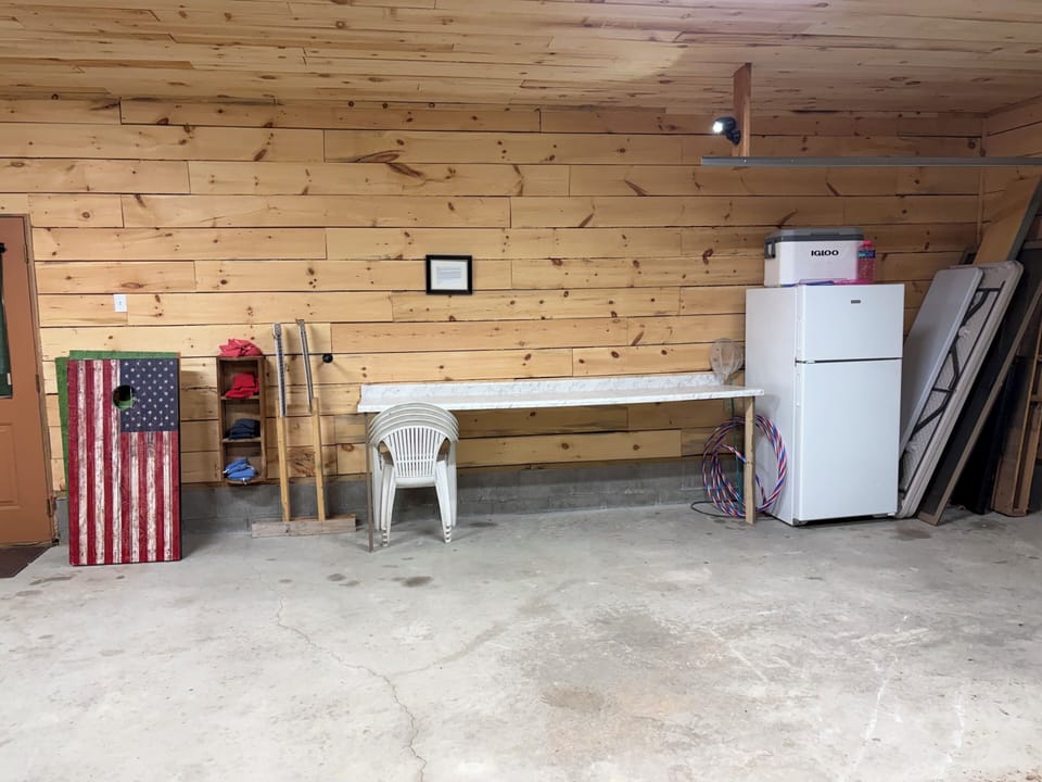 Garage with corn hole, buffet bench, extra fridge and folding tables.