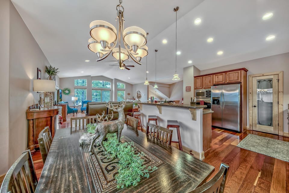 Dark wood dining table with deer centerpiece sits beside a granite breakfast bar and stainless steel kitchen appliances.