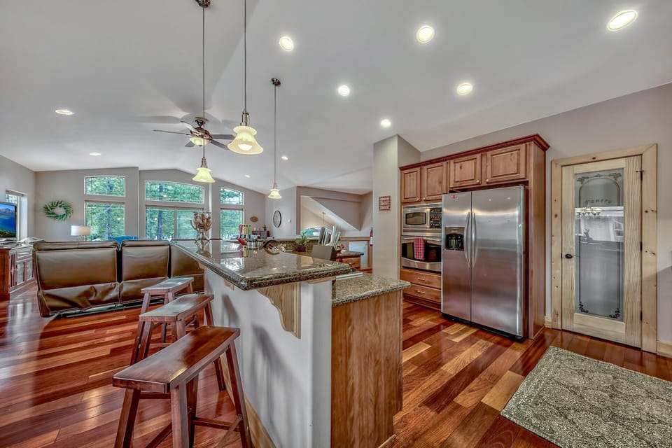 Granite-topped breakfast bar with wooden stools faces kitchen with stainless steel appliances and glass pantry door.