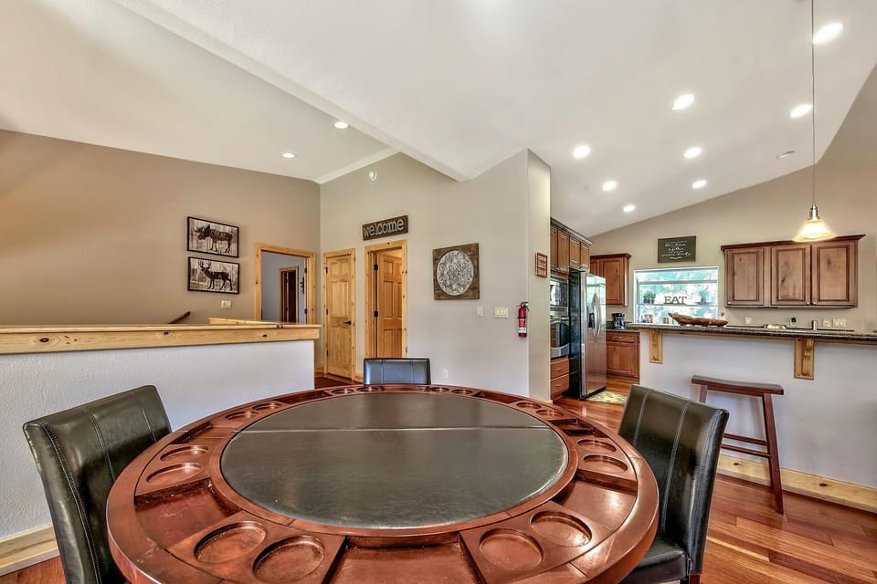 Round poker table with dark leather seats sits near a kitchen bar featuring granite counters and wood cabinetry.