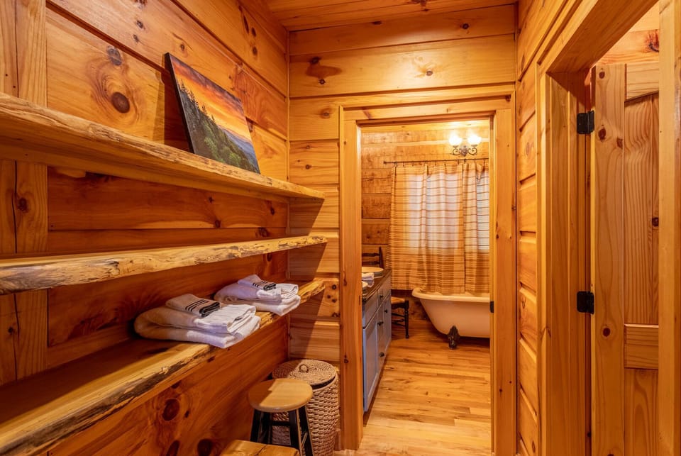 Rustic live-edge shelving stocked with fresh towels, just steps from a charming clawfoot tub bathroom.