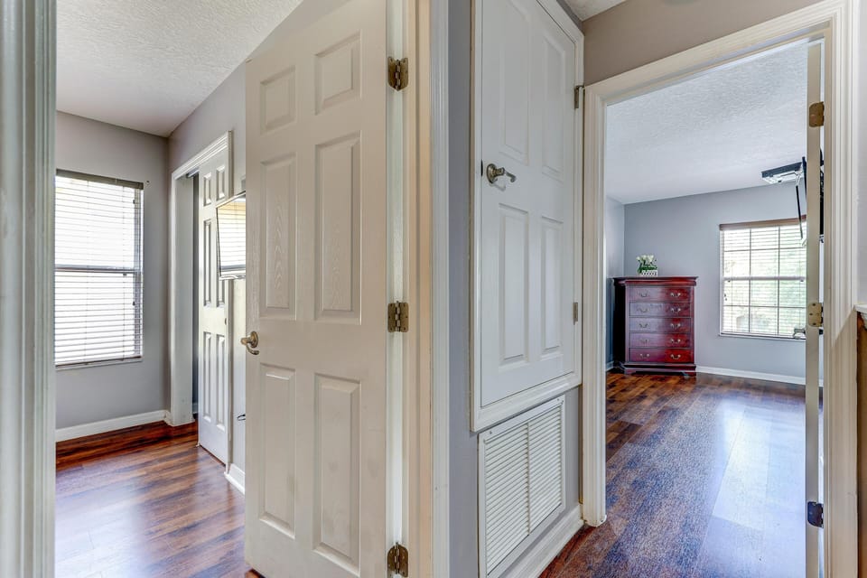 Entry to the bedroom with dark wood flooring, soft gray walls, white trim, and a tall mahogany chest beneath a window.