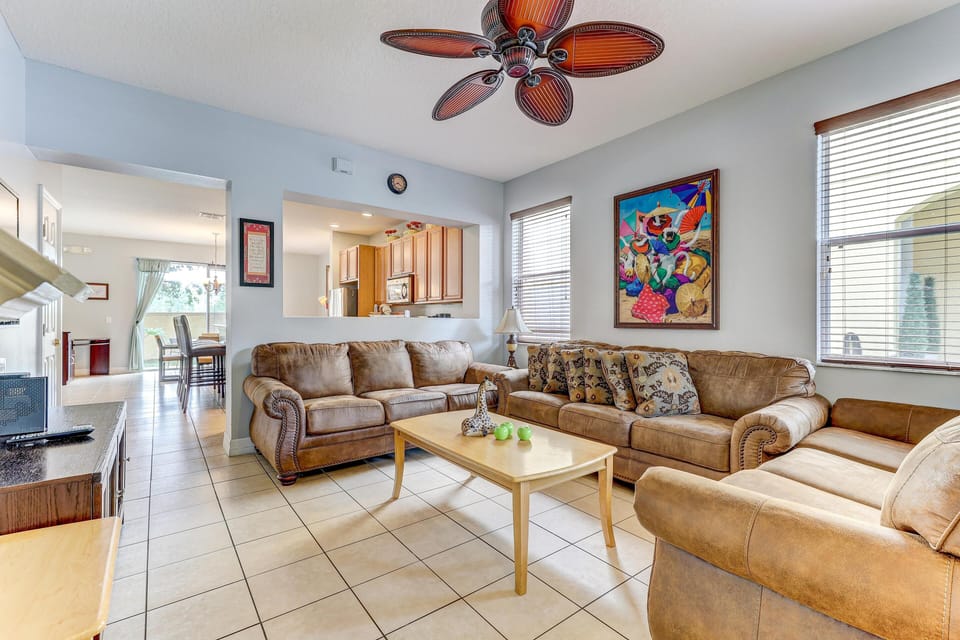 Sunlight filters through wooden blinds in the living room with leather sofas and a tropical ceiling fan.