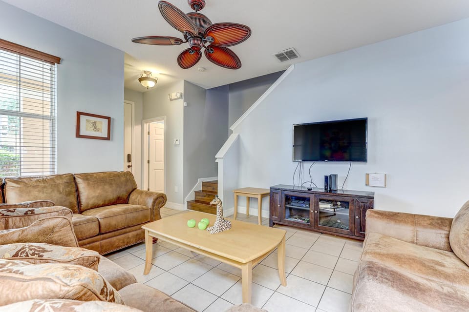 Neutral tile flooring anchors the living room with tan leather sofas, a pale wood coffee table, and a tropical ceiling fan.