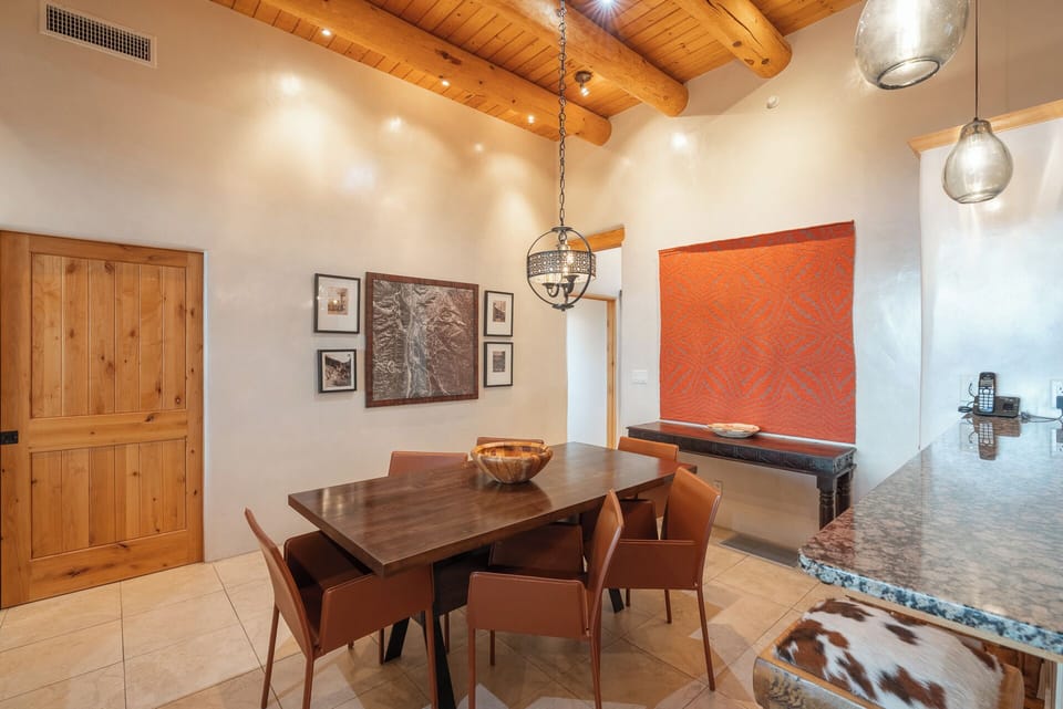 Gather around the dining table beneath soaring wood-beamed ceilings, where warm lighting and Southwestern-inspired décor create an inviting space for shared meals and conversation.