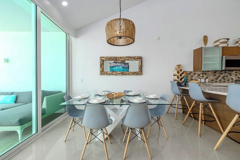 Picture yourself sharing meals at this airy dining space, where coastal charm meets modern comfort. Natural light pours through floor-to-ceiling windows, illuminating a stylish glass table ready for your group gatherings.