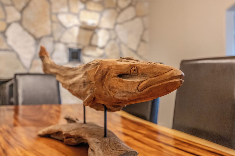 "Wooden fish sculpture centerpiece on dining table, set against a stone wall."