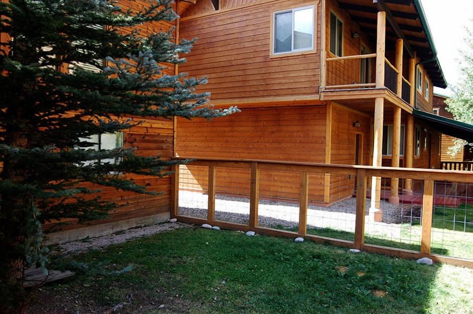 Three-story cedar-clad building surrounded by evergreen trees and manicured lawn, nestled in a natural forested setting.