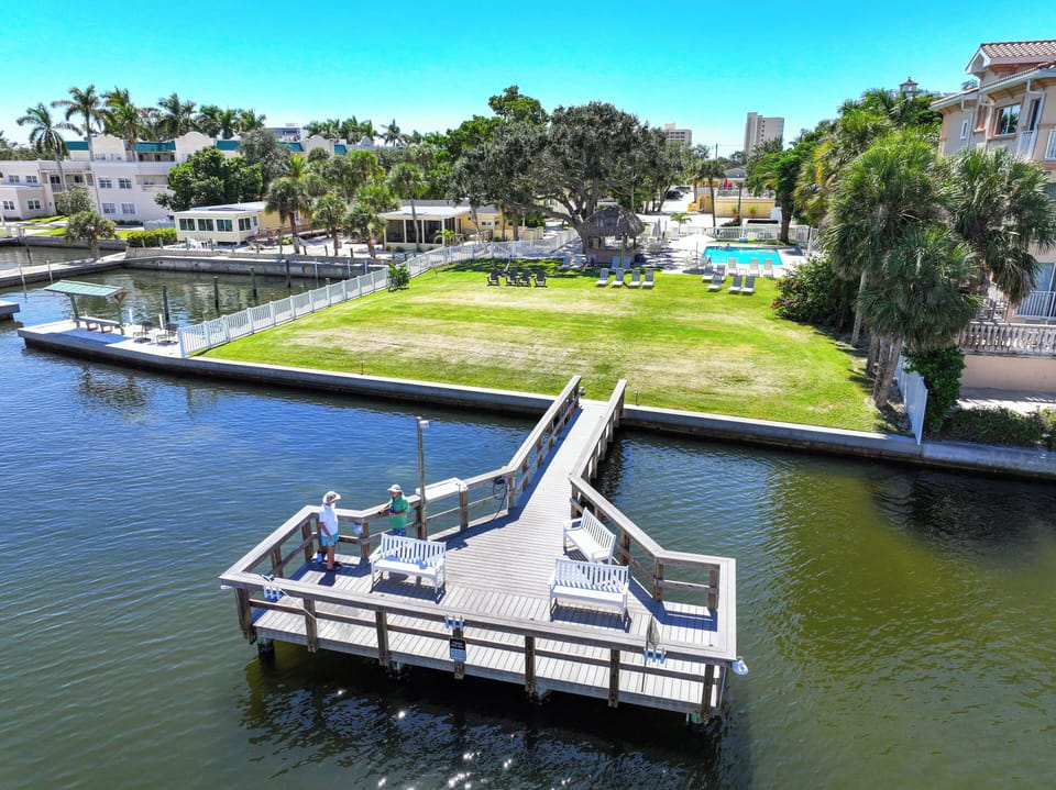 Aerial view of waterfront property featuring private dock on the canal, expansive lawn, and nearby access to local surroundings under clear blue skies.