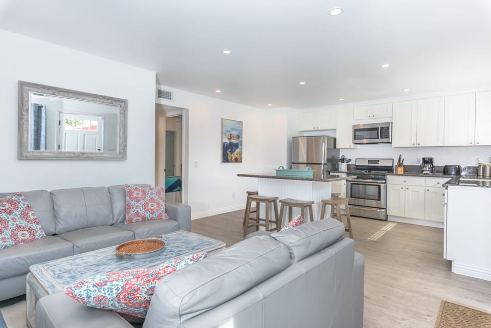 Front door opens up to the main living area, with a sofa set, cable TV, and open kitchen area.
                