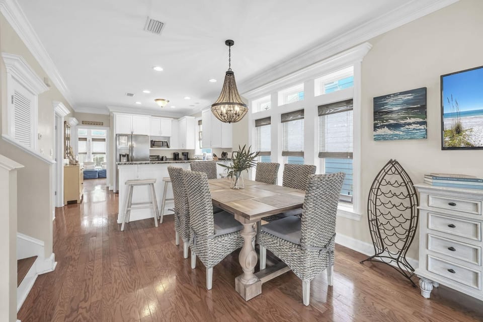 Dining area with woven chairs around a wooden table, hardwood floors, and a beaded chandelier overhead.