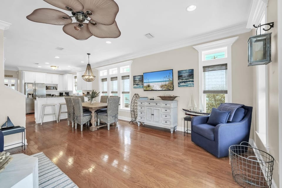 Open dining and living area with hardwood floors, wicker chairs, blue armchair, and coastal decor accents.