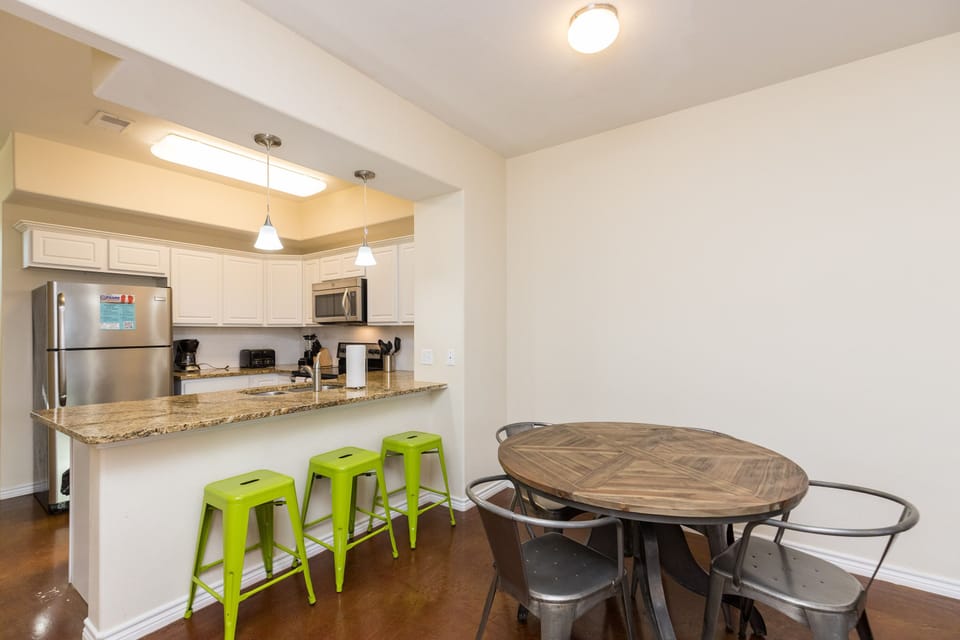 Your open-concept space seamlessly blends cooking and dining with granite counters, bright green stools, and a rustic round table for memorable meals.