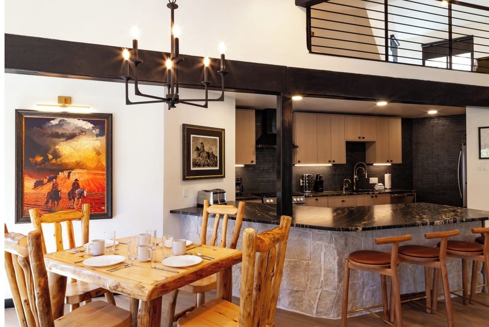 Step into your open-concept living space where rustic warmth meets modern comfort. Gather around the natural wood dining table, relax at the stone-clad breakfast bar, and enjoy the soaring ceilings and thoughtful design that make this your mountain retreat