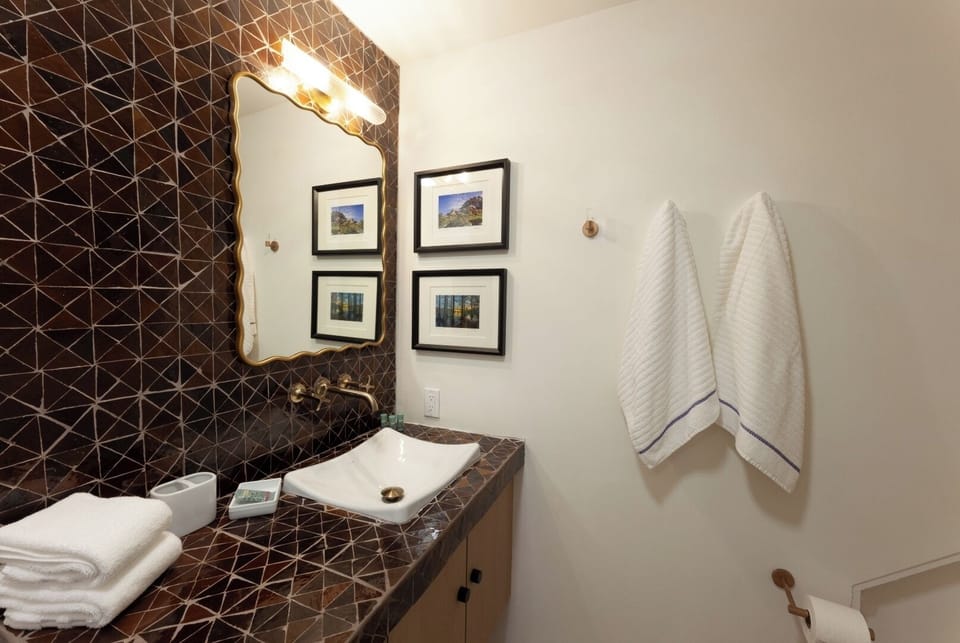 Step into your stylish bathroom featuring a striking geometric accent wall, modern sink, warm lighting, and curated artwork—fresh towels await your arrival.
