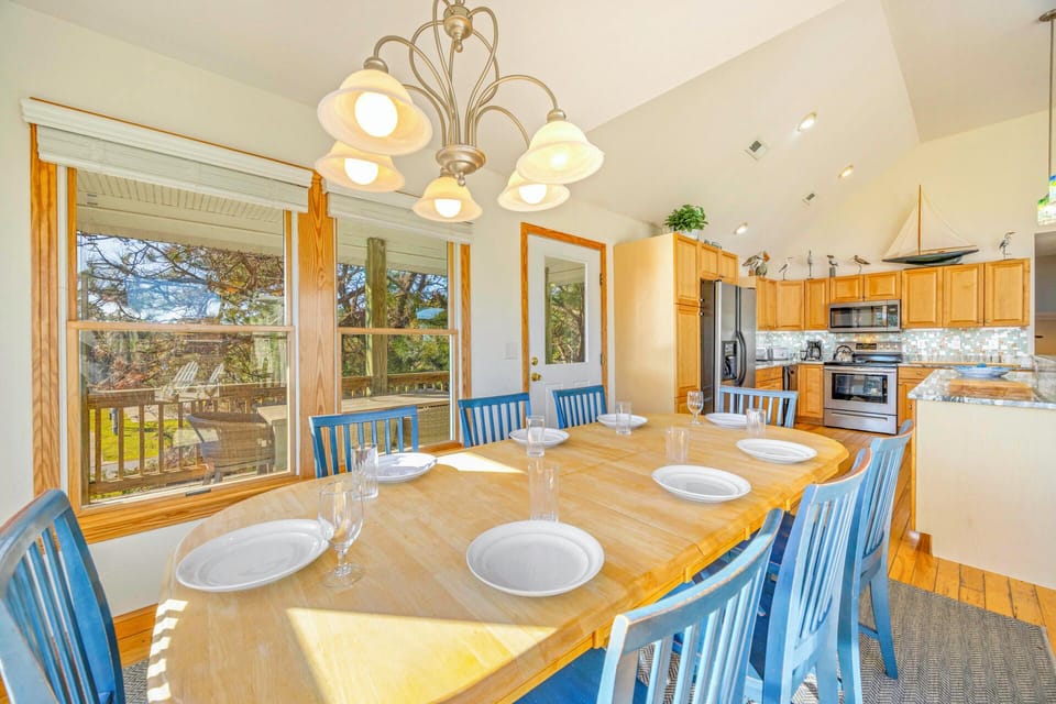 Gather around this inviting dining table where warm sunlight streams through large windows, creating the perfect spot for memorable meals with loved ones.
