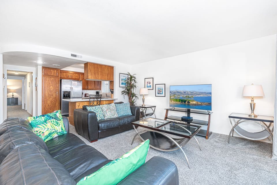View of main living spaces from the front entry. Open floor plan between living, kitchen and dining areas. Sliding glass doors open up to front, ocean view patio.
                