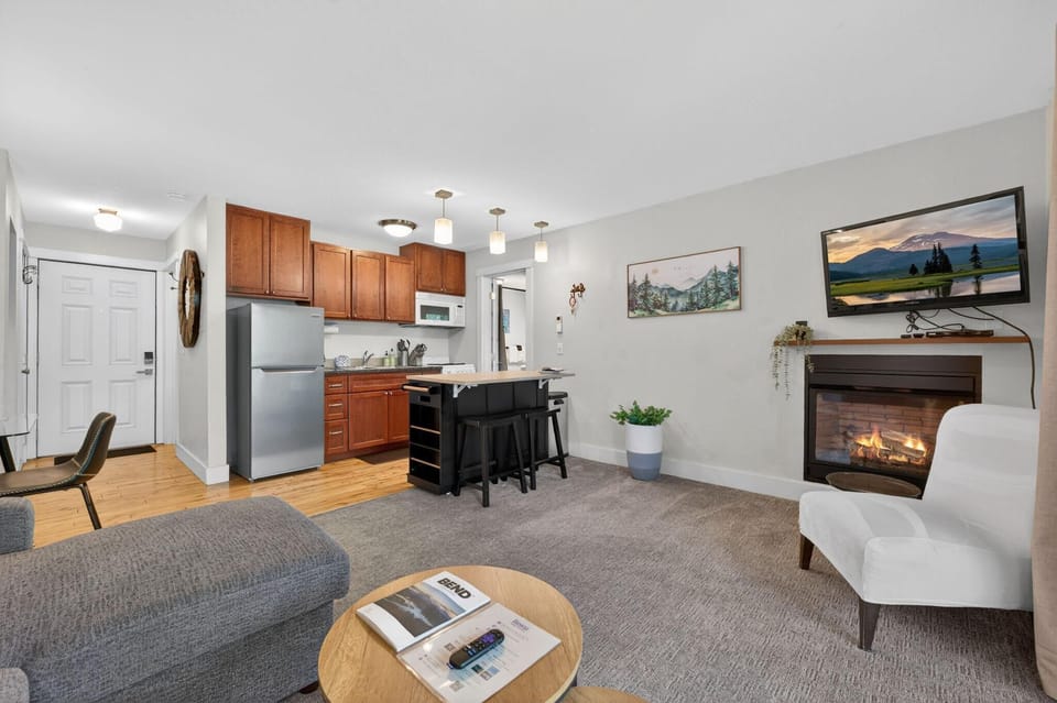 Open living area with gray sectional, gas fireplace beneath mounted TV, and kitchen island with wood countertop.