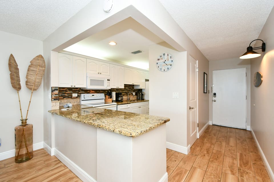 Modern, completely renovated kitchen with granite counter tops, glass tile back splash, opens to living/dining area and window/door overlooking the bay and boat docks