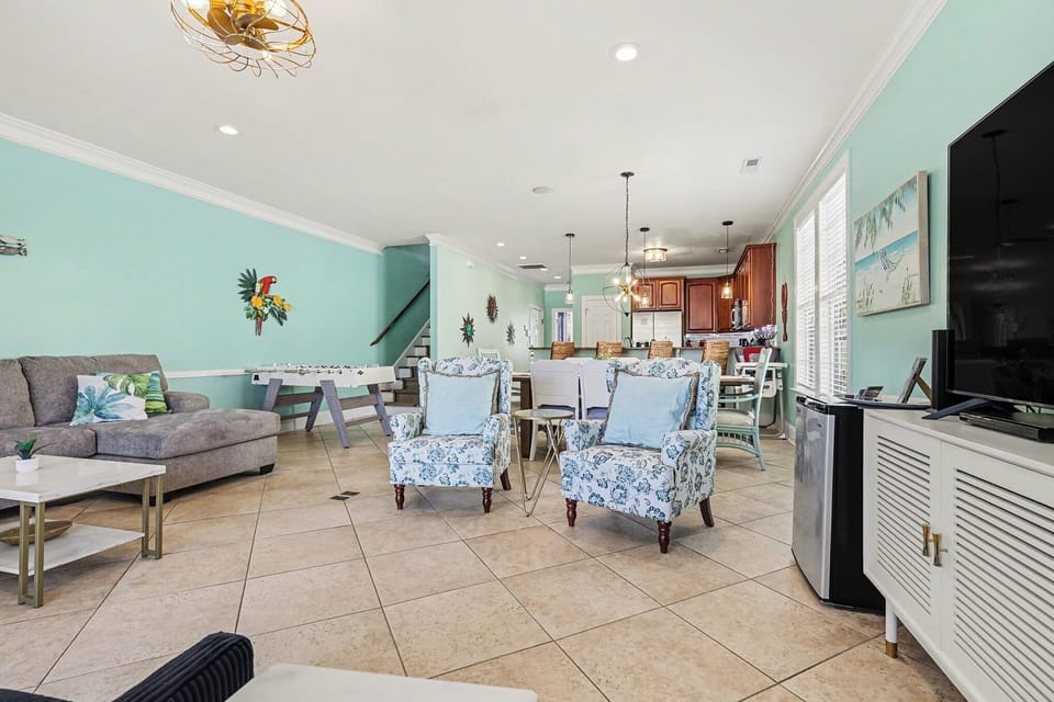 Spacious open-concept living area featuring stylish coastal furnishings, foosball table for fun nights in, and seamless flow to the kitchen and dining space.