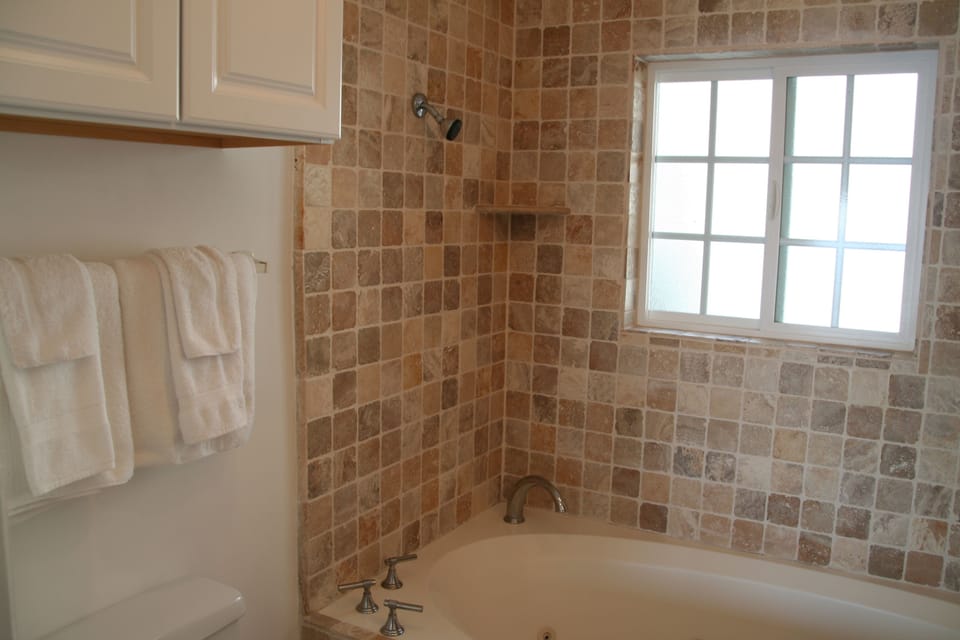 The full bathroom has a large Jacuzzi tub surrounded with travertine tile