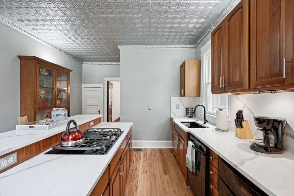 Bright kitchen with marble counters, wood cabinets, and tin ceiling charm.