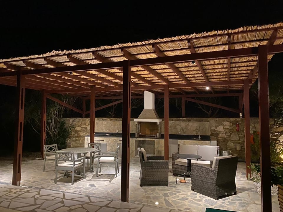 Night time view of outdoor kitchen with gas BBQ, charcoal/Wood grill and fridge
